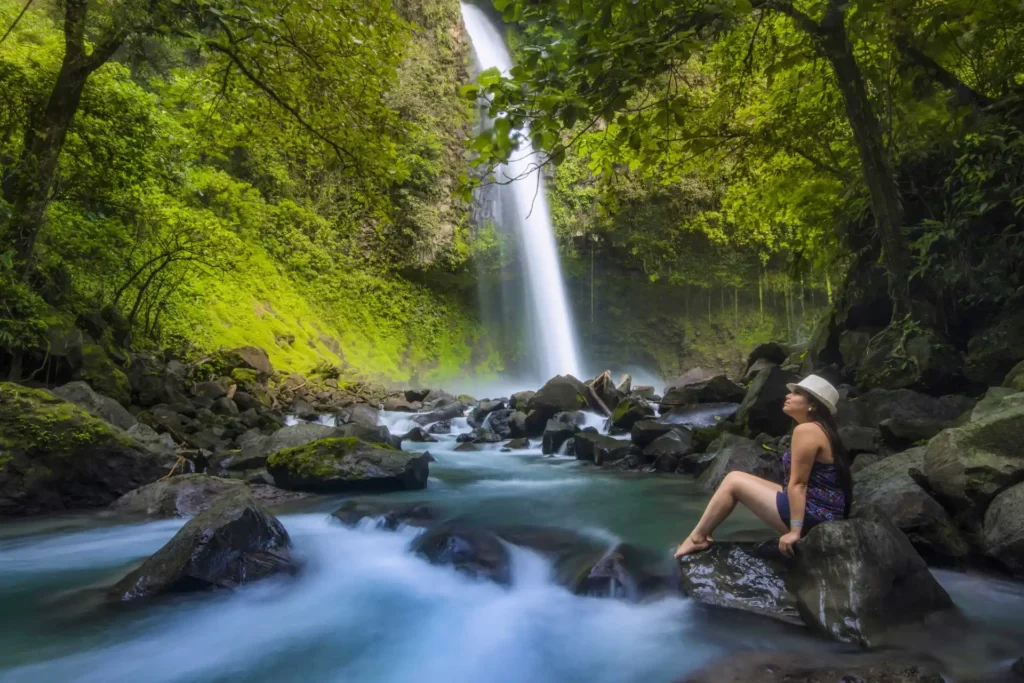 Frau sitzt am Fortuna Wasserfall in Costa Rica - nur eine von vielen Aktivitäten, die im Costa Rica Urlaub möglich sind! Noch Fragen? Katharina Fenners berät Sie persönlich!