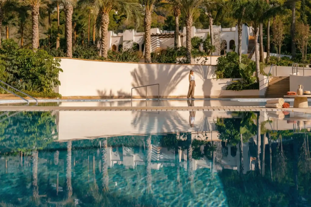 Eine Frau am glitzernden Wasser eines der Pools der ZEM Wellness Clinic Altea bei Alicante. Die Architektur dieses 5-Sterne-Grand Longevity-Hotels garantiert eine intime und ruhige Atmosphäre. Katharina Fenners gestaltet Ihren maßgeschneiderten Aufenthalt.