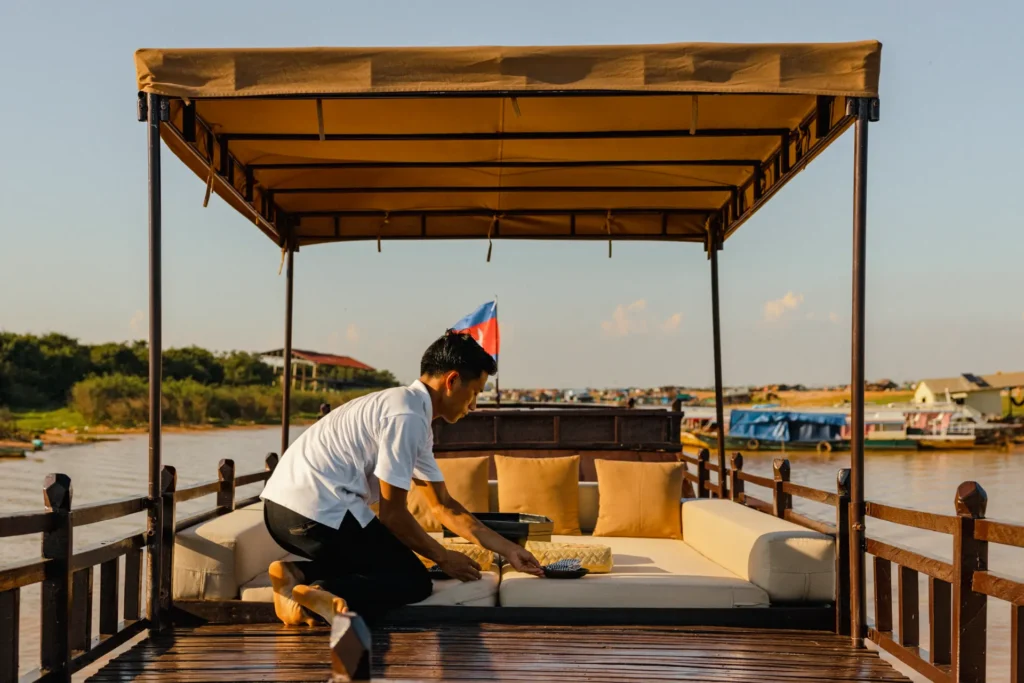 Ein Hotelangestellter verwöhnt Gäste während einer privaten Amansara Bootstour über den Tonle Sap. Buchbar bei Fenners Reisen, auch im Rahmen einer maßgeschneiderten Kambodscha Rundreise!