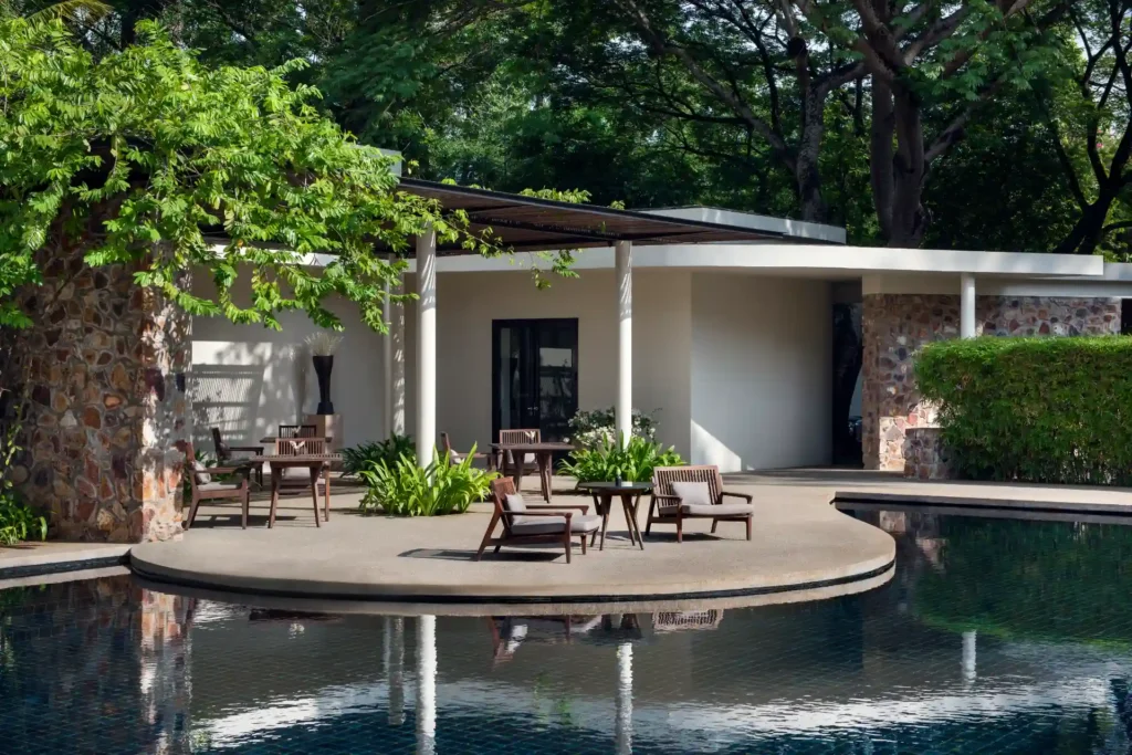 Der geschwungene Hauptpool des Amansara Luxusresorts in Kambodscha wird wie. das intime Refugium durch die klare Formensprache der New-Khmer-Architektur der 1960er-Jahre geprägt. Buchbar ist der Aufenthalt bei Fenners Reisen - auch im Rahmen einer individuellen Rundreise durch Kambodscha!