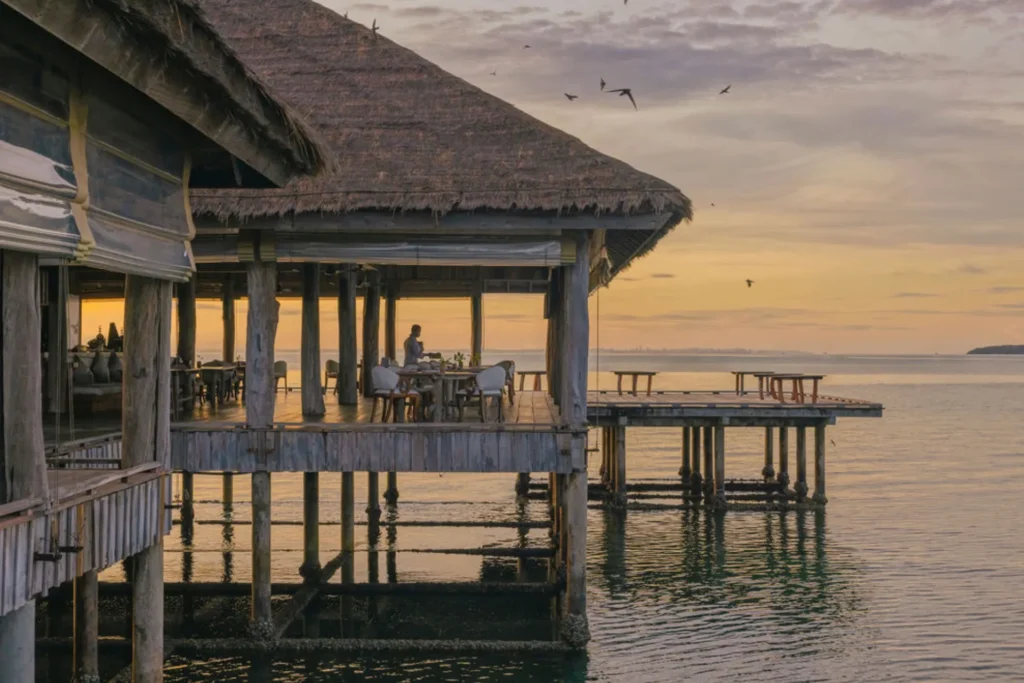 Restaurant auf Stelzen über dem Wasser im Sonnenuntergang. Sp speist man auf Song Saa Private Island in Kambodscha, buchbar bei Fenners Reisen.